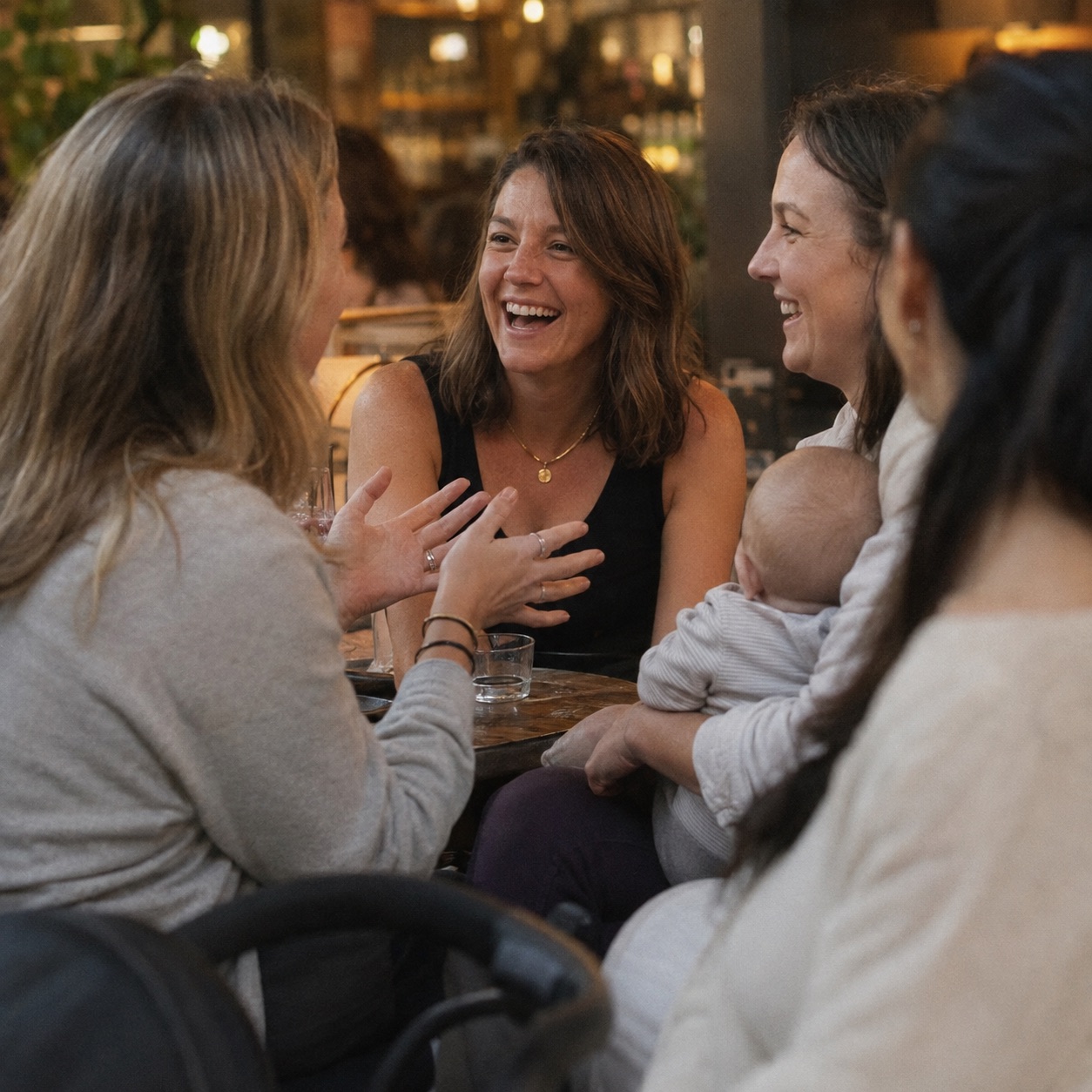 New mums laughing around a café table, one holding her baby